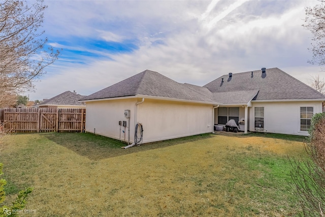 rear view of house featuring roof with shingles, fence, a lawn, and stucco siding