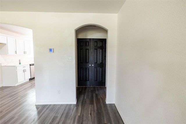 corridor featuring wood finished floors, arched walkways, and baseboards