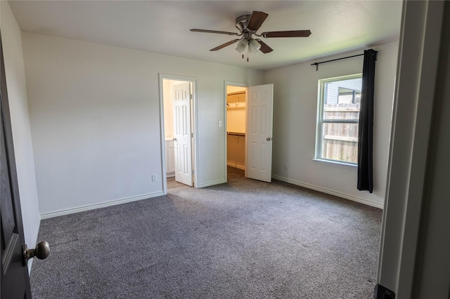unfurnished bedroom featuring a walk in closet, ceiling fan, carpet, and baseboards
