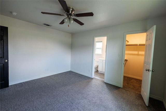 unfurnished bedroom featuring a closet, a walk in closet, visible vents, dark carpet, and baseboards