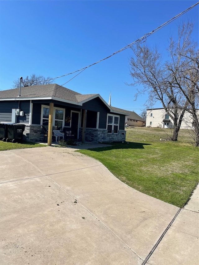 view of front of house featuring stone siding, a shingled roof, and a front lawn