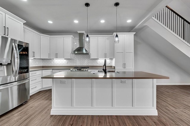 kitchen featuring dark countertops, stainless steel fridge with ice dispenser, a sink, wood finished floors, and wall chimney exhaust hood