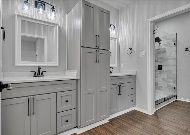 full bathroom featuring wood finished floors, a stall shower, two vanities, and a sink