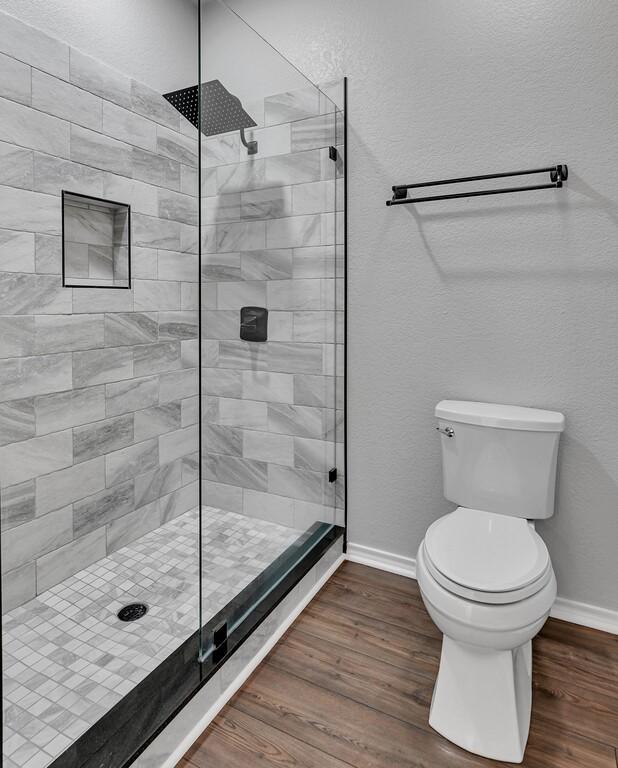 full bath with toilet, baseboards, wood finished floors, and tiled shower