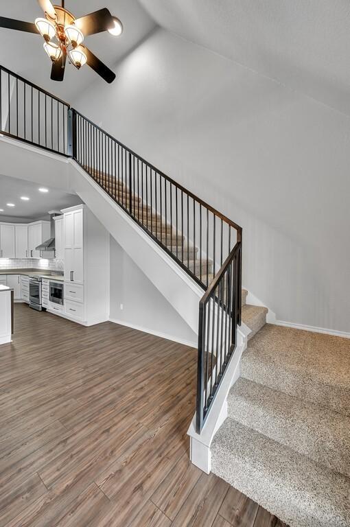 stairs featuring a ceiling fan, baseboards, high vaulted ceiling, and wood finished floors