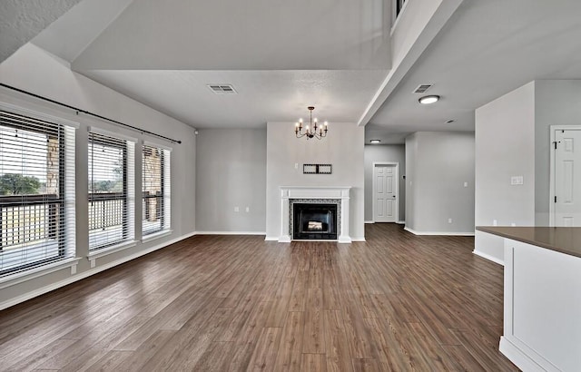 unfurnished living room featuring visible vents, baseboards, dark wood finished floors, a fireplace with flush hearth, and a notable chandelier