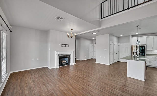 unfurnished living room featuring dark wood-style floors, a fireplace, visible vents, and a notable chandelier