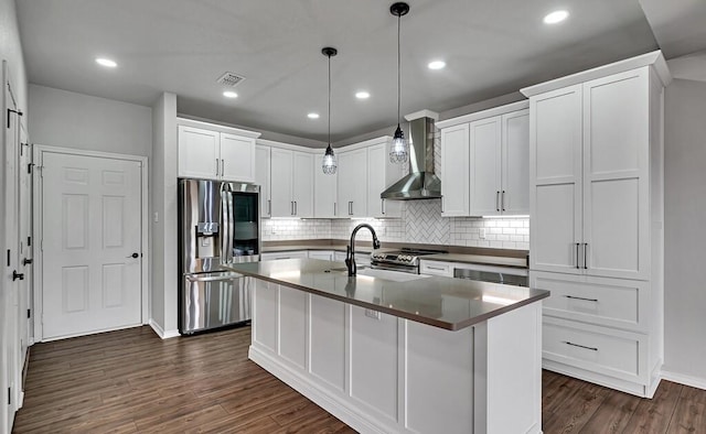 kitchen featuring a kitchen island with sink, dark wood-type flooring, white cabinets, appliances with stainless steel finishes, and wall chimney range hood