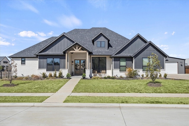 modern farmhouse with a shingled roof, a front yard, french doors, and brick siding