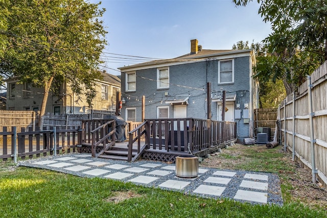 rear view of house with brick siding, a chimney, central AC unit, a fenced backyard, and a wooden deck