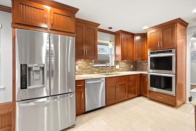 kitchen featuring tasteful backsplash, brown cabinets, light stone countertops, stainless steel appliances, and a sink