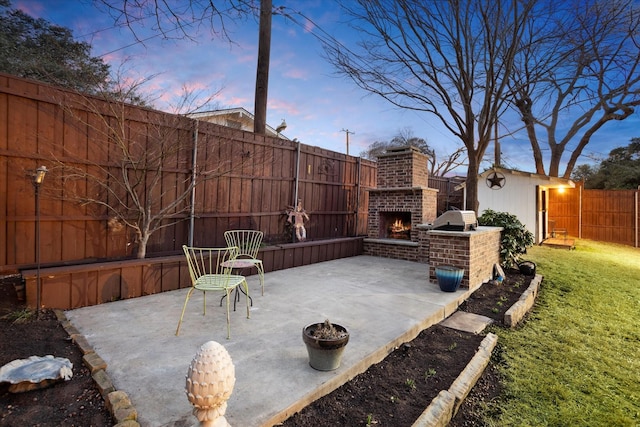 view of patio featuring an outdoor brick fireplace, an outbuilding, and a fenced backyard