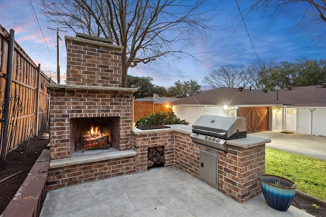 patio terrace at dusk featuring exterior kitchen, an outdoor brick fireplace, grilling area, and a fenced backyard