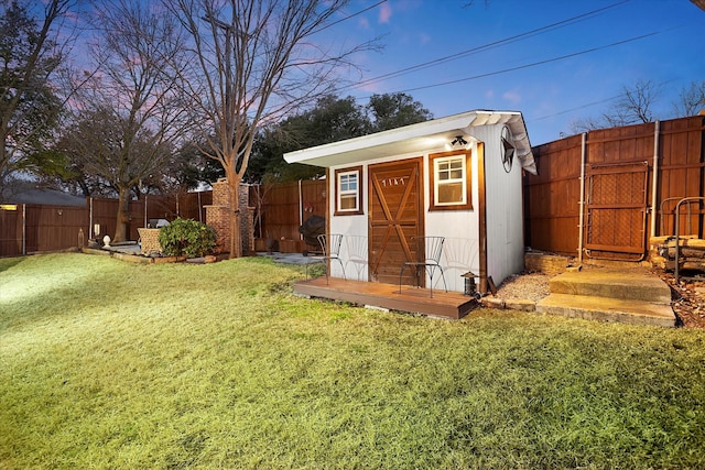 outdoor structure at dusk with a fenced backyard, a storage unit, a lawn, and an outdoor structure