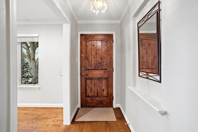 foyer entrance featuring baseboards, ornamental molding, a chandelier, and wood finished floors