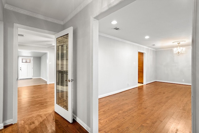 spare room with crown molding, visible vents, an inviting chandelier, wood finished floors, and baseboards