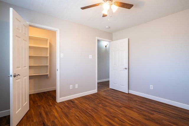 unfurnished bedroom with a ceiling fan, a walk in closet, baseboards, and wood finished floors