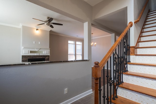 stairs with a fireplace, baseboards, crown molding, and ceiling fan with notable chandelier