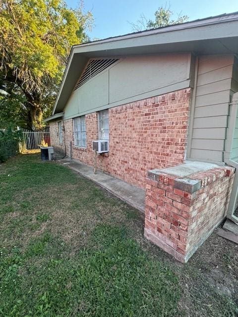 view of side of property with a yard, brick siding, cooling unit, and fence