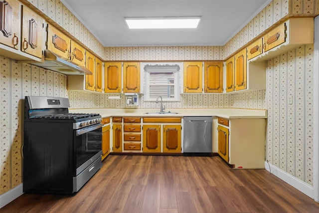 kitchen with wallpapered walls, dark wood finished floors, appliances with stainless steel finishes, under cabinet range hood, and a sink