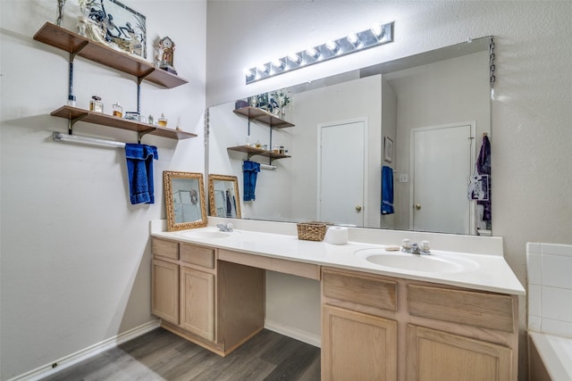 bathroom featuring wood finished floors, baseboards, double vanity, a tub, and a sink