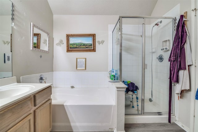 bathroom with a textured ceiling, wood finished floors, a shower stall, a bath, and vanity