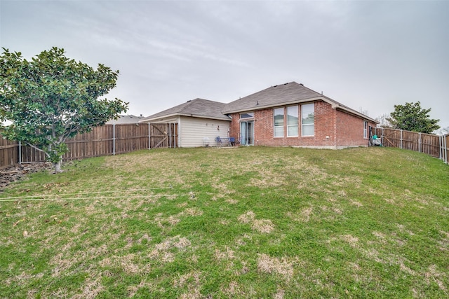 rear view of property featuring brick siding, a fenced backyard, and a lawn