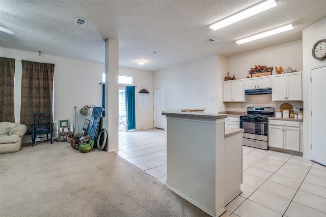 kitchen featuring visible vents, stainless steel range with gas stovetop, light colored carpet, light tile patterned flooring, and white cabinetry