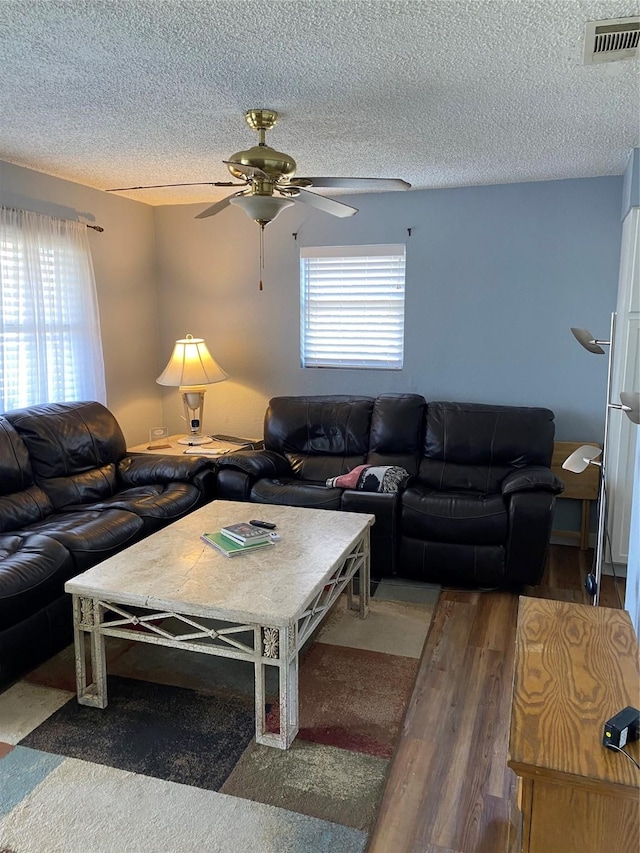 living area featuring visible vents, a textured ceiling, wood finished floors, and a ceiling fan