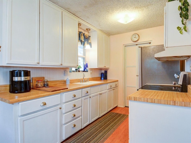 kitchen with light wood-style floors, white cabinets, a sink, and a textured ceiling