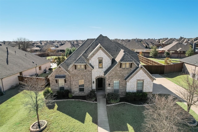 french country home with a front lawn, a shingled roof, fence, and brick siding