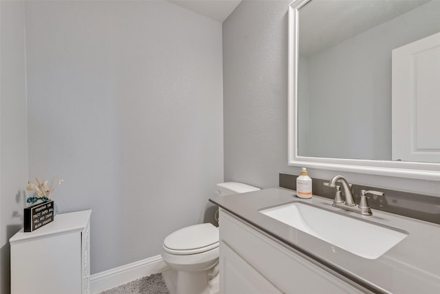 half bath featuring baseboards, vanity, and toilet