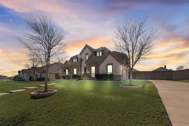 french provincial home with a front yard, fence, a garage, stone siding, and driveway