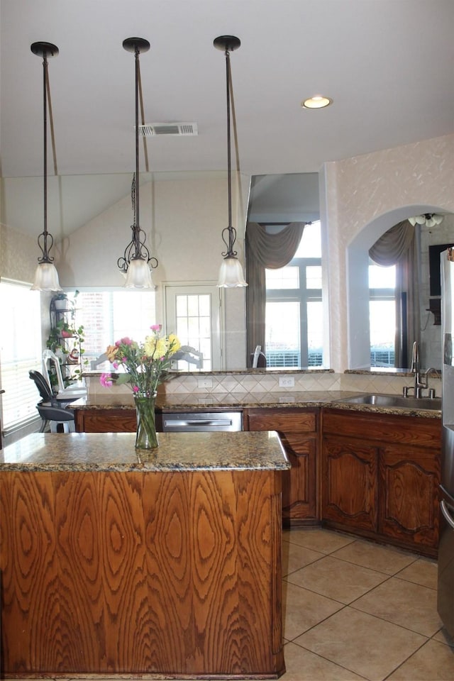 kitchen featuring visible vents, appliances with stainless steel finishes, brown cabinetry, a sink, and a kitchen island