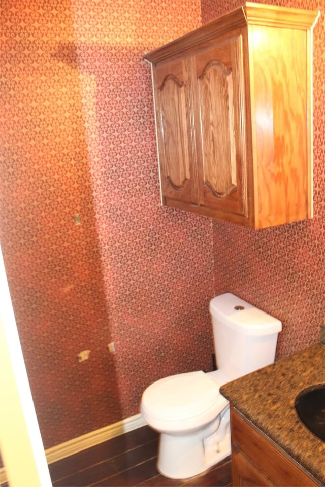 half bathroom with baseboards, vanity, toilet, and wood finished floors