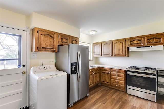 kitchen featuring brown cabinetry, washer / clothes dryer, dark wood-type flooring, stainless steel appliances, and under cabinet range hood