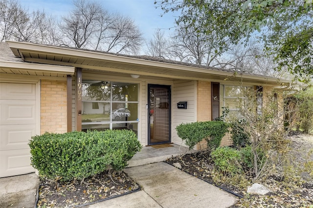 doorway to property featuring a garage and brick siding