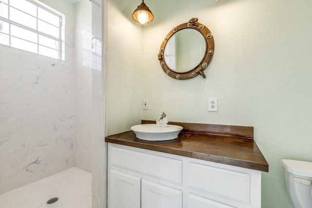 full bath with a textured wall, vanity, toilet, and walk in shower