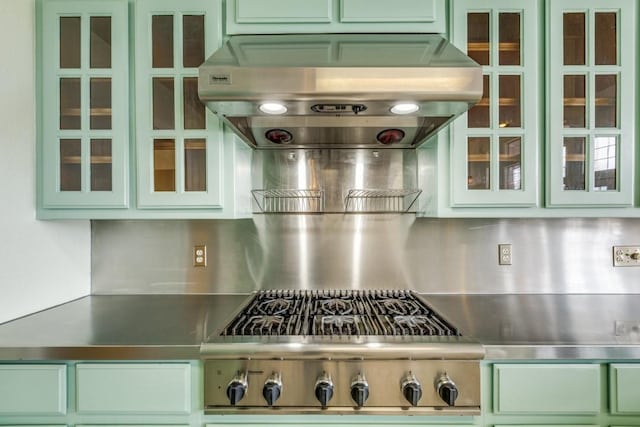 kitchen featuring range, stainless steel countertops, glass insert cabinets, green cabinets, and exhaust hood