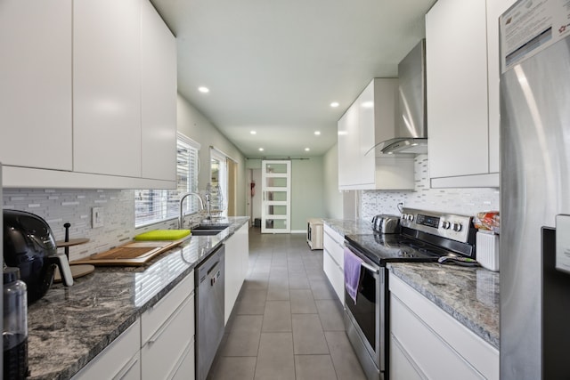 kitchen with a sink, white cabinetry, appliances with stainless steel finishes, tile patterned floors, and wall chimney exhaust hood