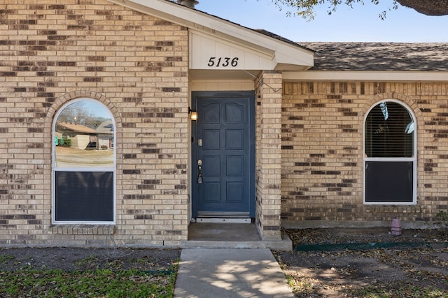 view of exterior entry with roof with shingles and brick siding