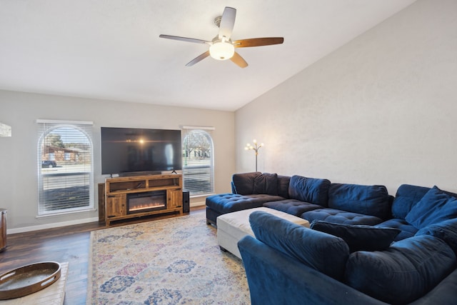 living area featuring lofted ceiling, a healthy amount of sunlight, a glass covered fireplace, and wood finished floors