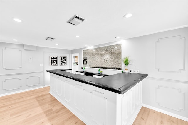 kitchen featuring light wood finished floors, dark countertops, visible vents, a decorative wall, and white cabinets