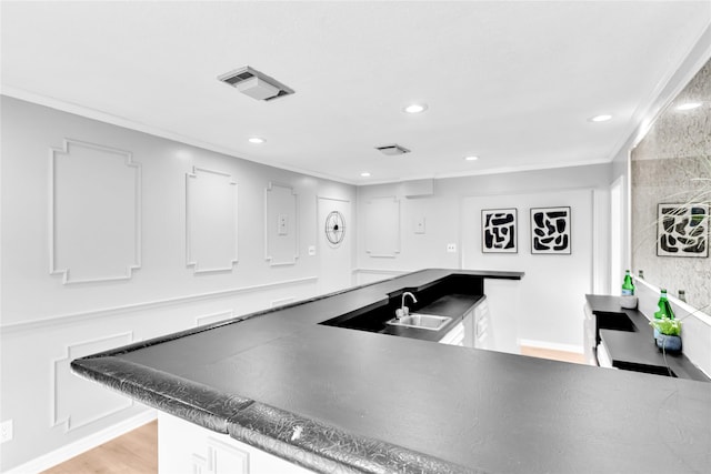 kitchen featuring recessed lighting, visible vents, light wood-style flooring, ornamental molding, and a sink