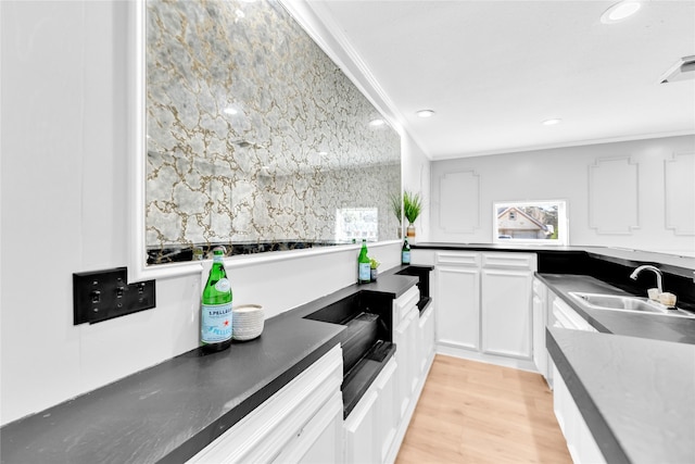 kitchen with light wood finished floors, crown molding, white cabinetry, and a sink