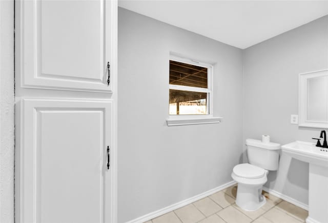 half bathroom with tile patterned floors, toilet, and baseboards