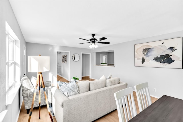 living area featuring light wood-style floors, ceiling fan, and baseboards