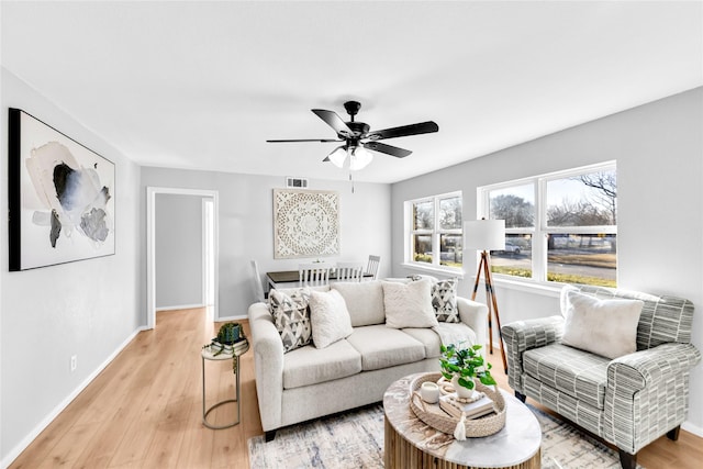 living room with light wood-type flooring, baseboards, visible vents, and ceiling fan