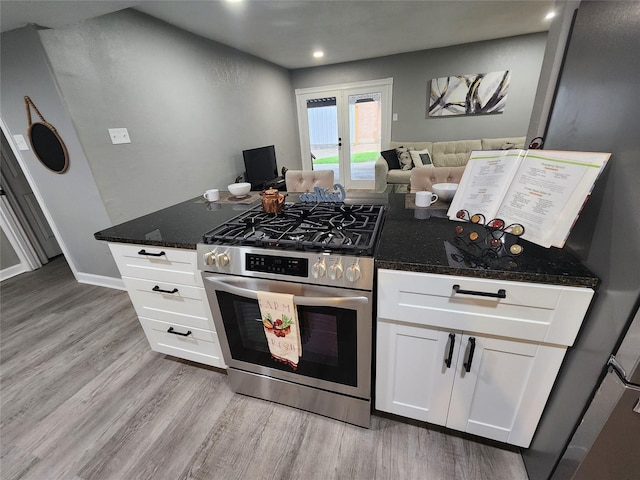 kitchen with light wood finished floors, stainless steel gas range oven, white cabinets, dark stone counters, and recessed lighting