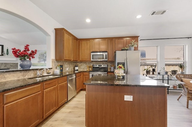 kitchen featuring stainless steel appliances, a sink, visible vents, backsplash, and dark stone countertops